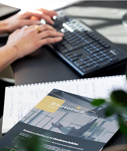 Medarbejder skriver på tastatur ved siden af kursusmateriale fra Rhetorica